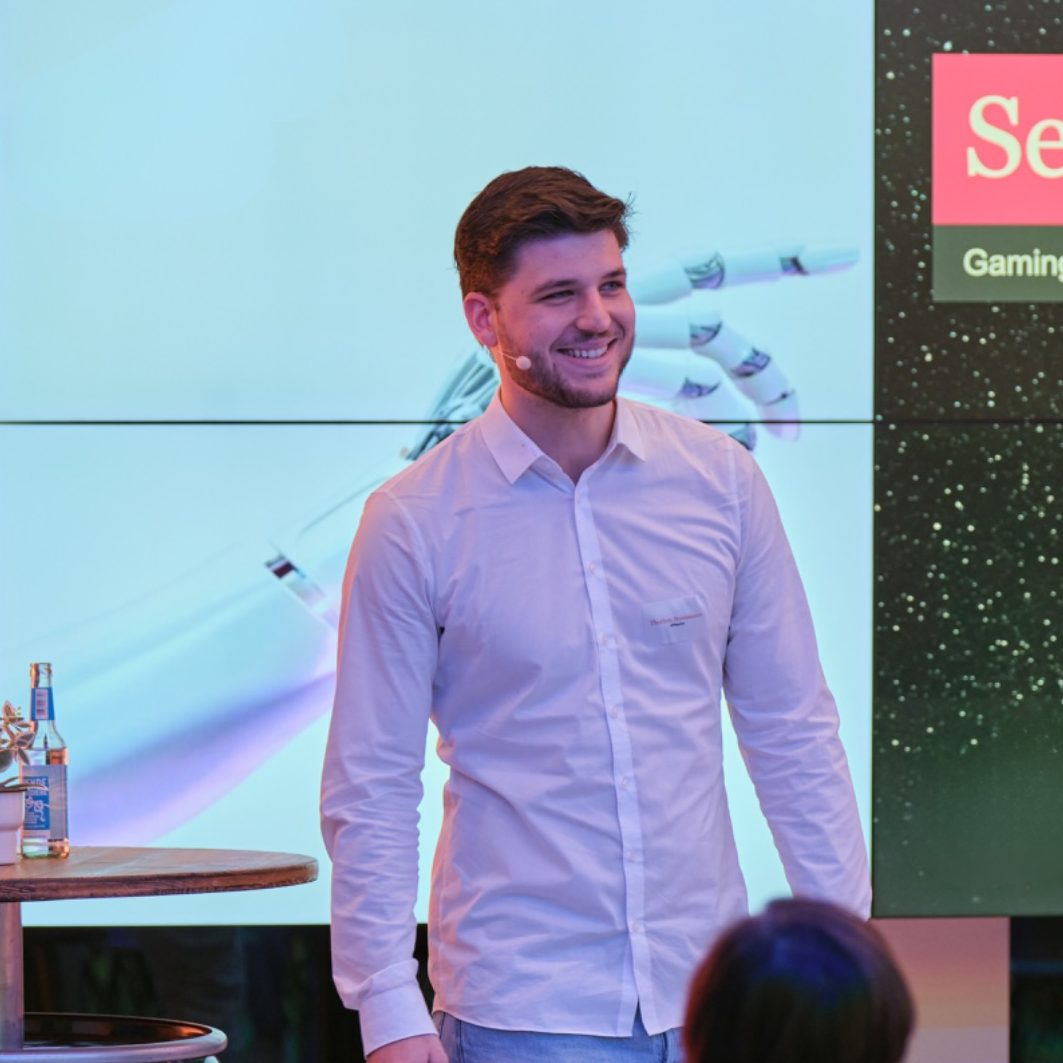 Thorben Steenmanns, ein Serious Gaming Experte, steht vor einem Bildschirm bei einem Event auf der er einen Vortrag hält über Gaming.