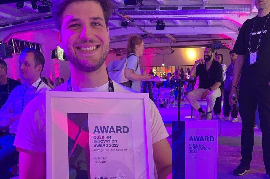 Lächelnder Mann hält ein Zertifikat mit der Aufschrift "Award" in einer Veranstaltung.